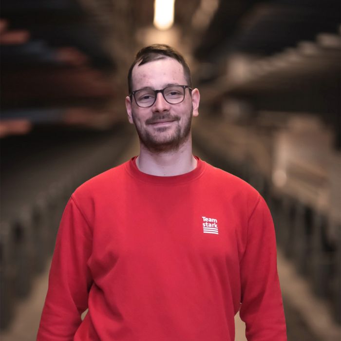 Stark AG Mitarbeiter Mitarbeiter der Stark AG in einem roten Pullover steht in einem Lagerhaus.
