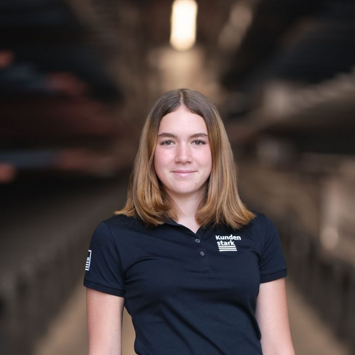 Mitarbeiterin der Stark AG Junge Frau in Stark AG Uniform vor unscharfem Lagerhintergrund.